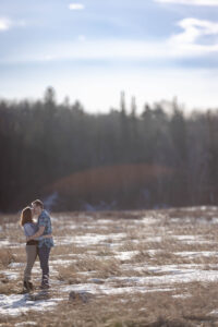 engaged couple standing in field hugging