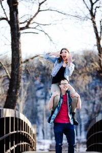 woman on mans shoulder pointing happlily at engagement ring