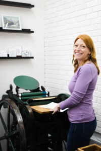 designer standing by Chandler and Price platen press in studio