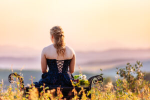 calgary high school grad sitting on wrought iron bench in field during golden hour