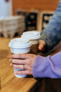 The couple stands at a quaint café counter, close up photo of engagement ring as they receive steaming cups of hot chocolate.