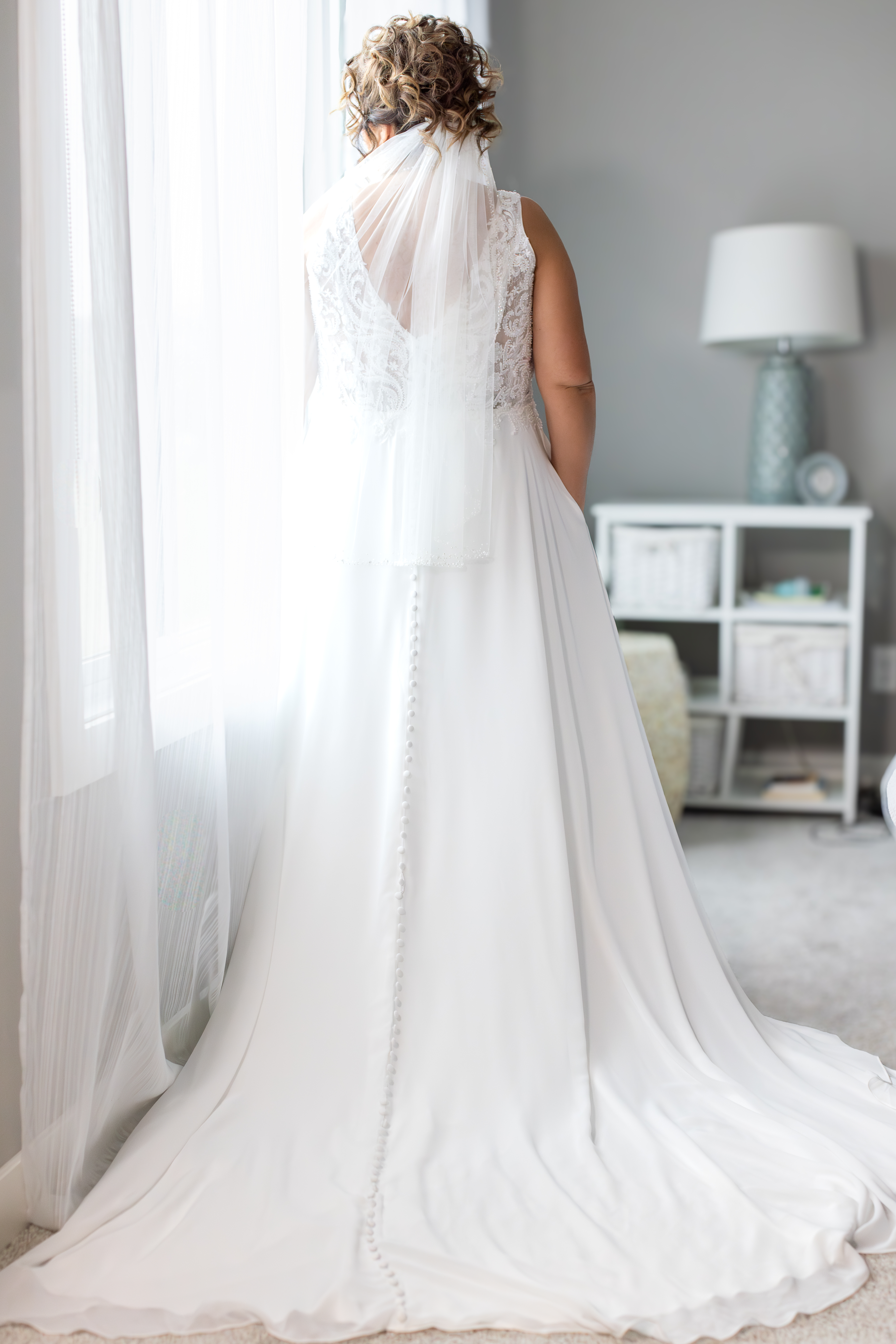 Bride in Calgary wedding dress standing by window with dramatic natural light on rainy wedding day