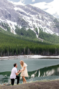 Engaged couple standing beside mountain lake in Kananaskis Alberta